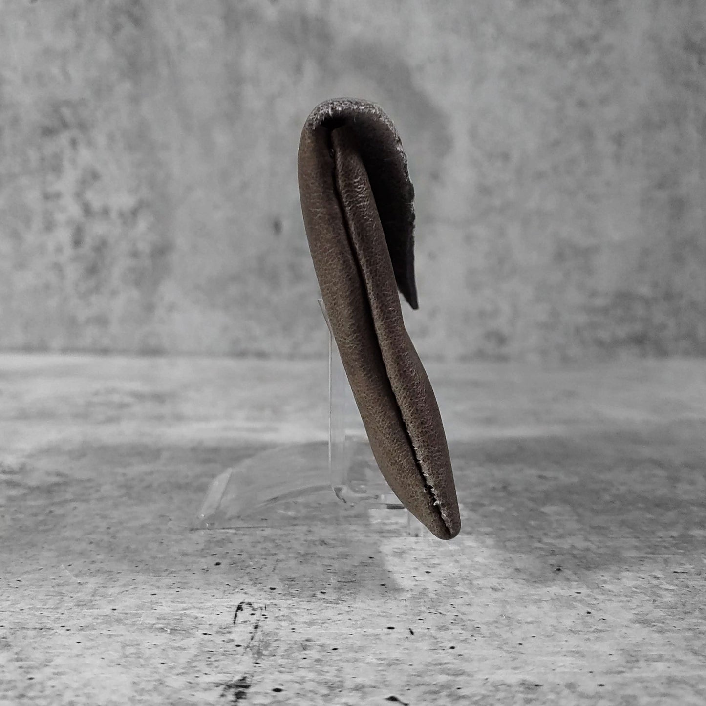 Side facing view of "smooth soft leather card holder" in iron against a concrete background.