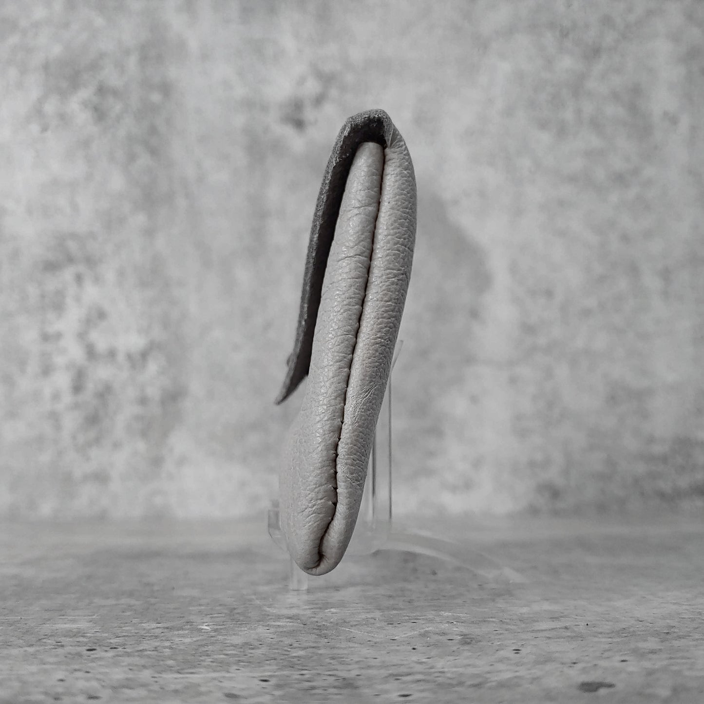 Side facing view of "soft leather card holder" in concrete grey against a concrete background.
