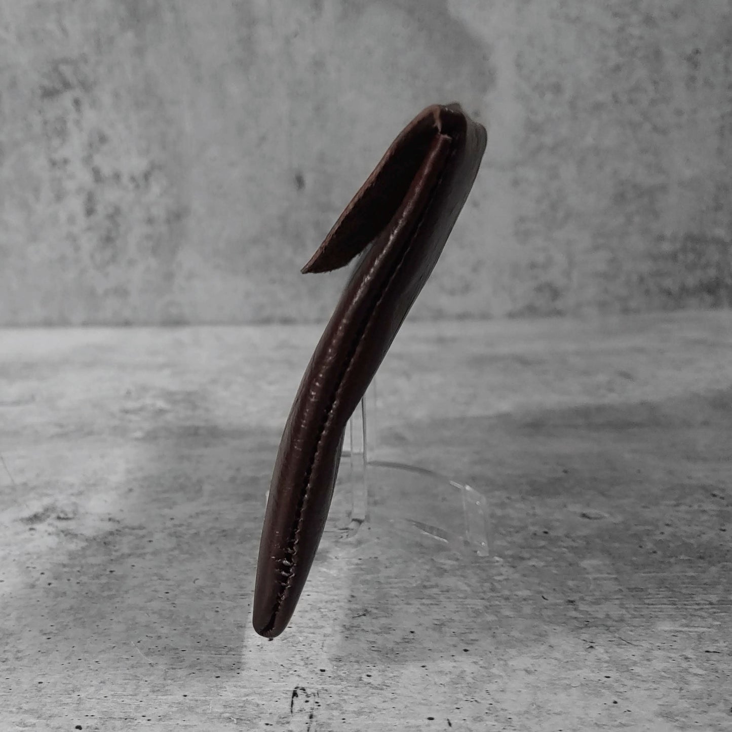Side view of "soft leather clutch trapezoid" in chocolate against a concrete background.