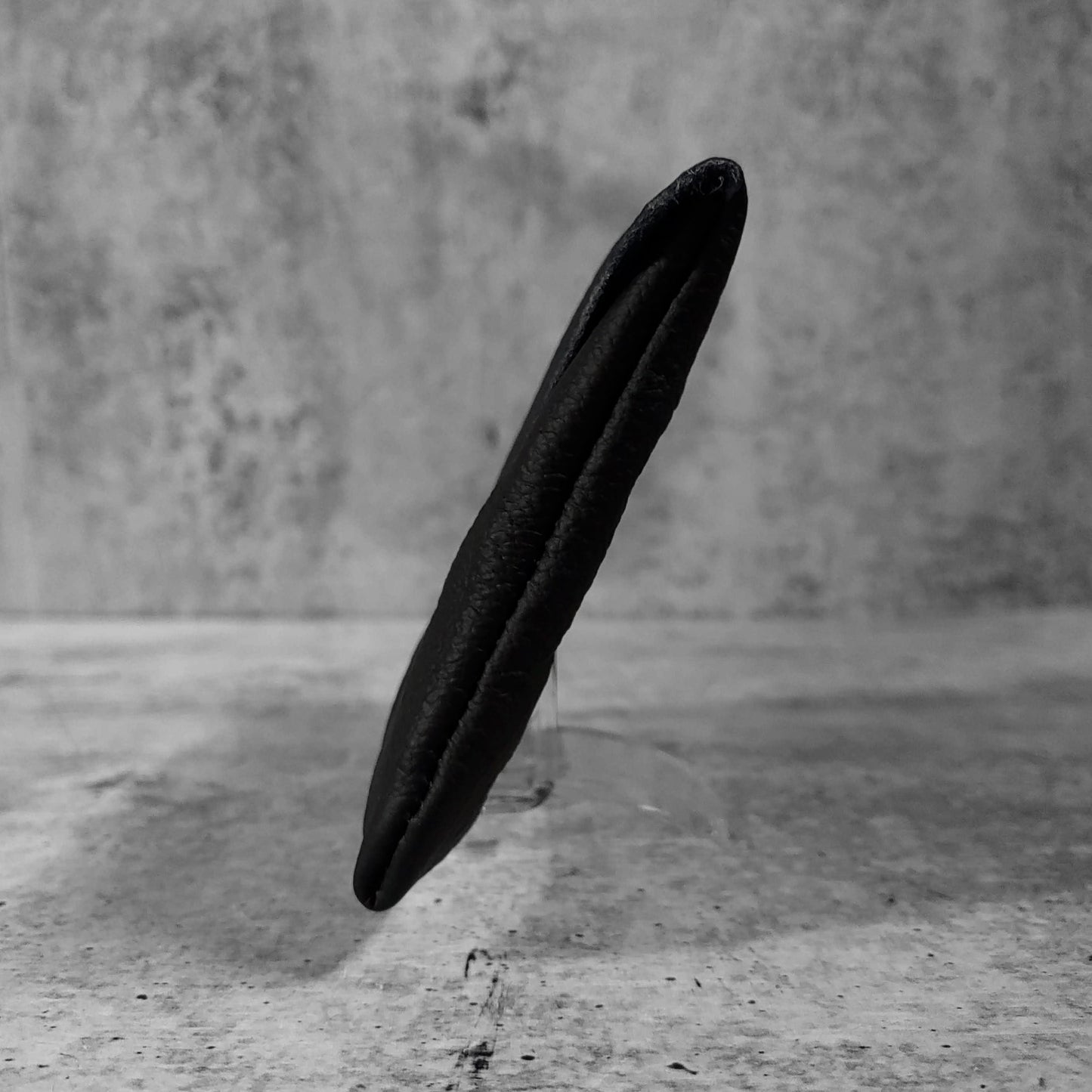 Side view of "soft leather clutch trapezoid" in onyx against a concrete background.