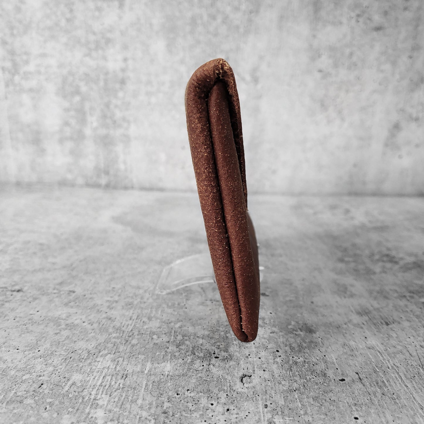 Side view of "soft leather clutch trapezoid" in walnut against a concrete background.