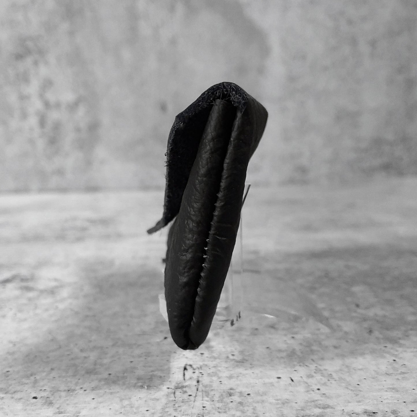 Side view of "wrinkled soft leather card holder" in onyx against a concrete background.