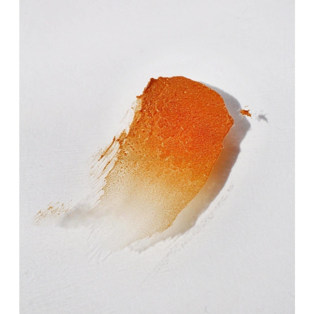 Shimmering golden NOTO Gold Glow Stick product smudged against white surface to showcase texture and pigment.