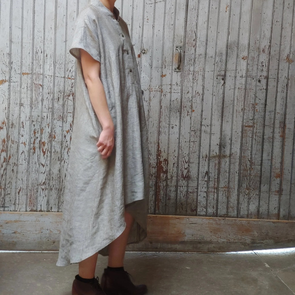 Side view of model in McCULLOUGH High Low Henley Tunic in silver textured linen. Model tugging on fabric slightly.