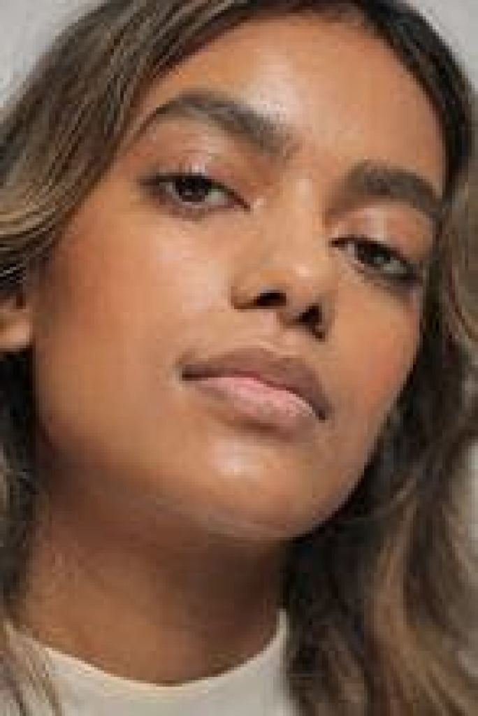 Translucent tan color NOTO Hydra Highlighter Stick product showcased on medium-dark skinned female around eyes and on cheeks.