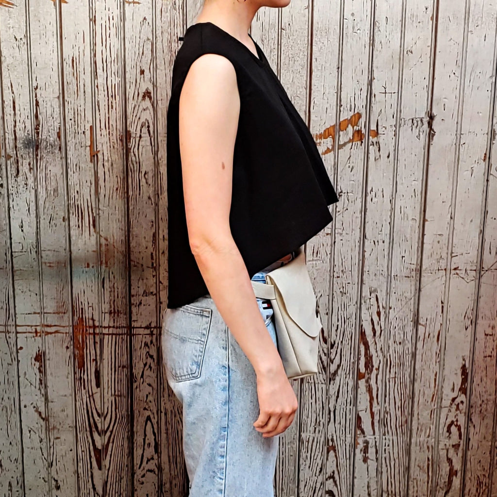 Side view of model wearing "large smooth leather hip bag" in off white against a wood paneled background.