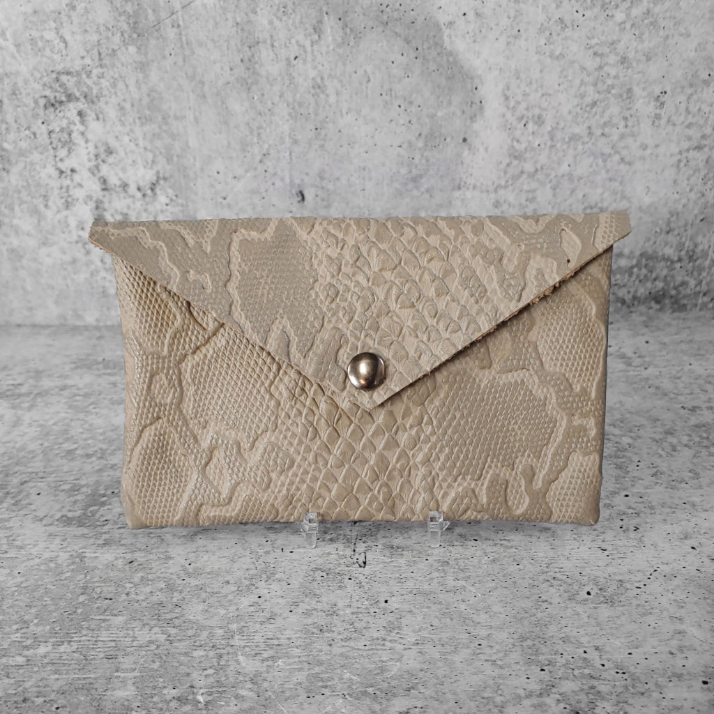 Front facing view of "leather clutch triangle" in dovetail against a concrete background.