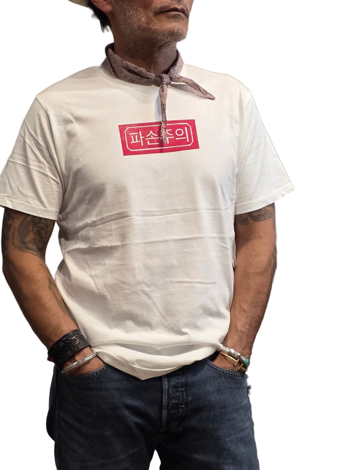 Man wearing a white t-shirt with a red logo and dark jeans standing on a textured floor.