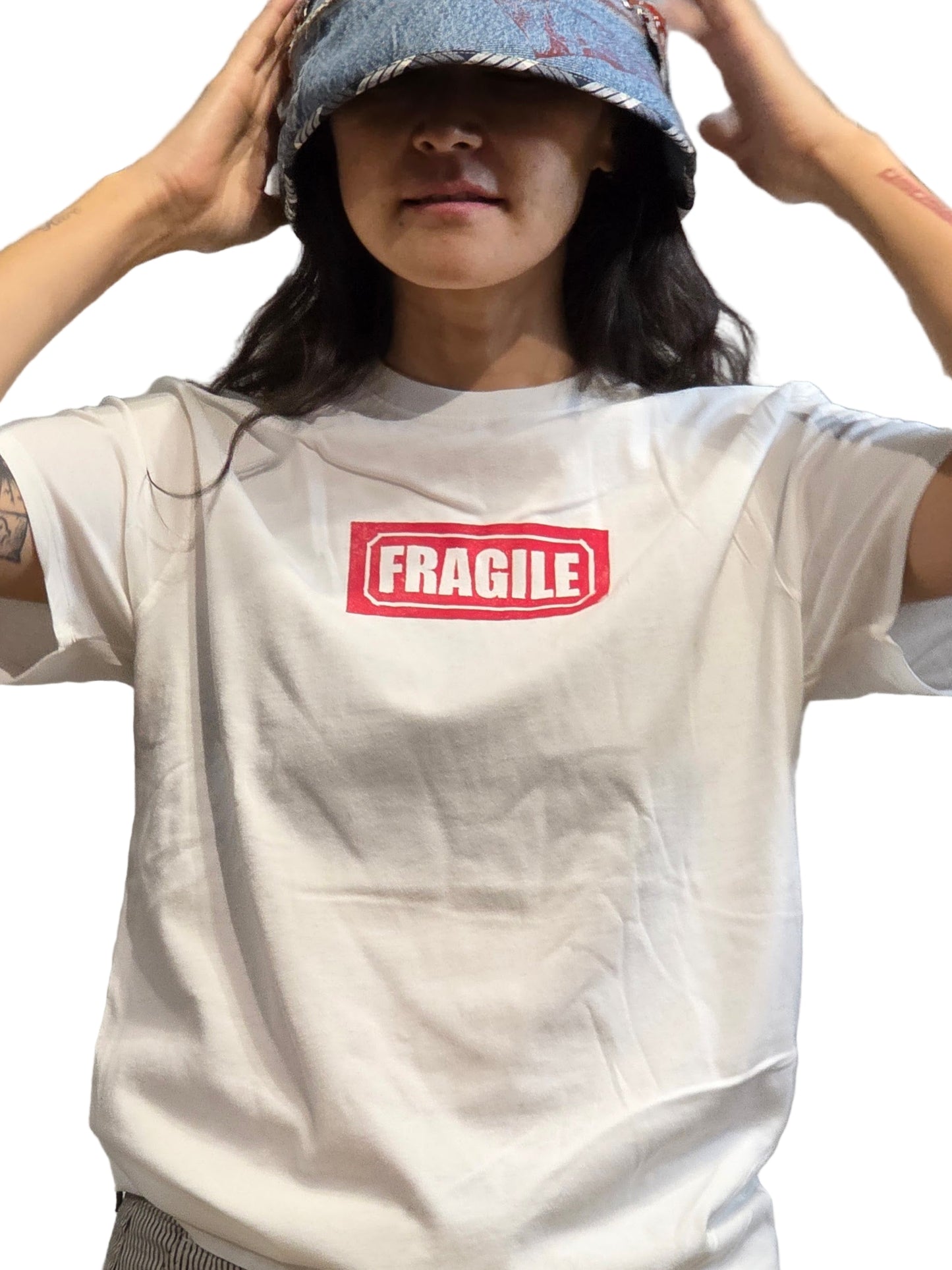 Person wearing a white t-shirt with 'FRAGILE' print in front of a neutral background from the MKWArt x McCullough Collaboration at Harkensback in Dallas, TX