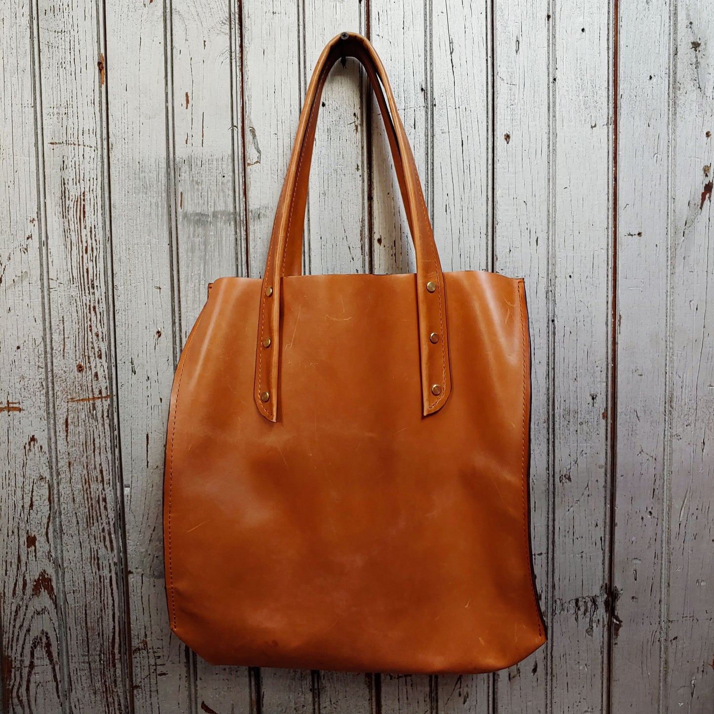 Front facing view of "large leather tote" in camel against a wood paneled background.