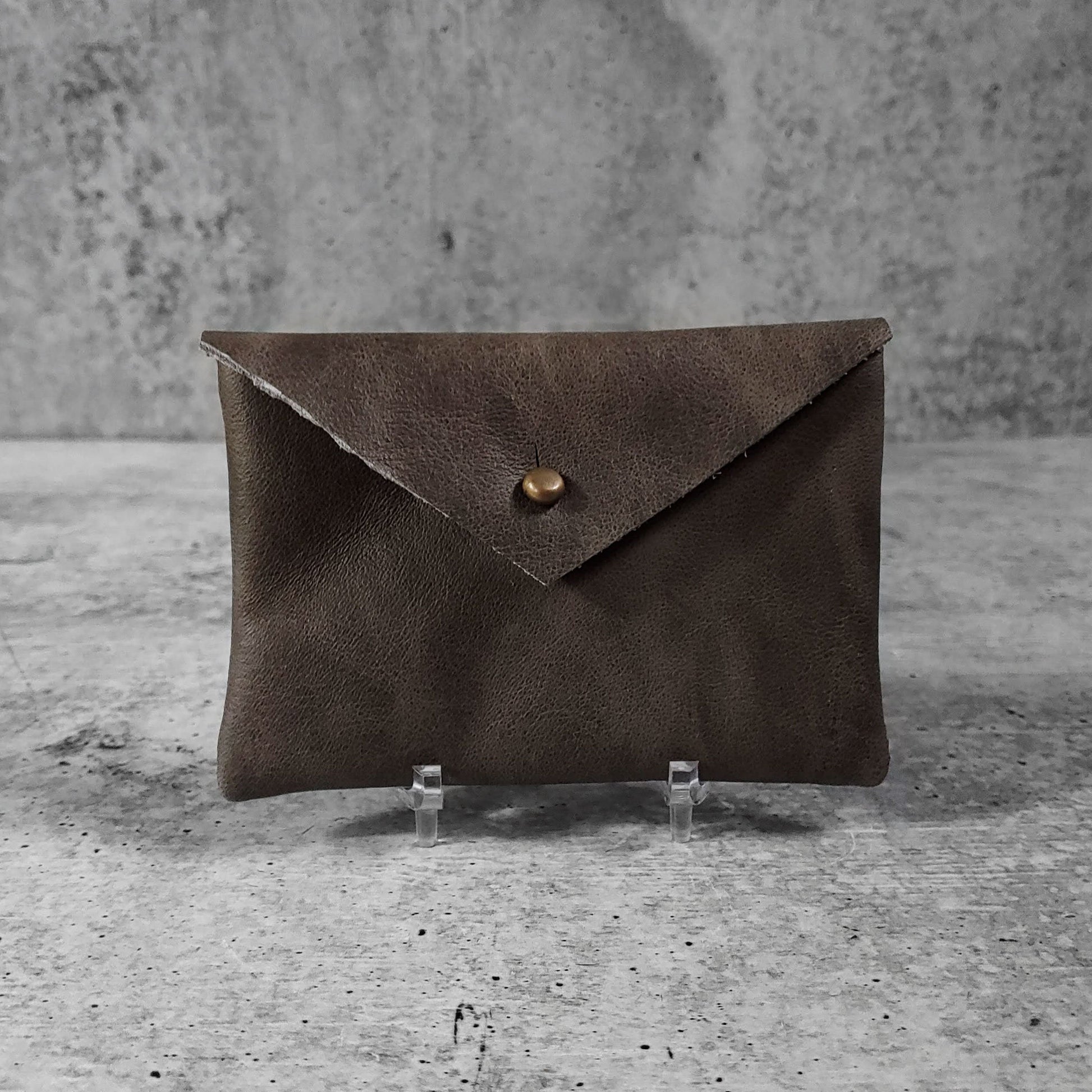Front facing view of "smooth soft leather card holder" in iron against a concrete background.