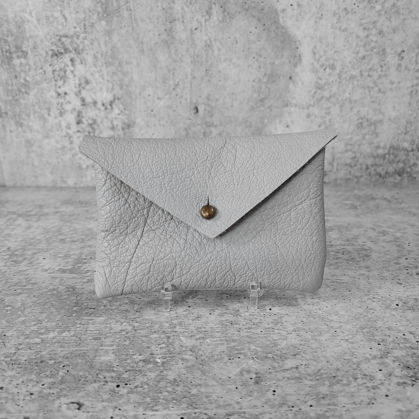 Front facing view of "soft leather card holder" in concrete grey against a concrete background.