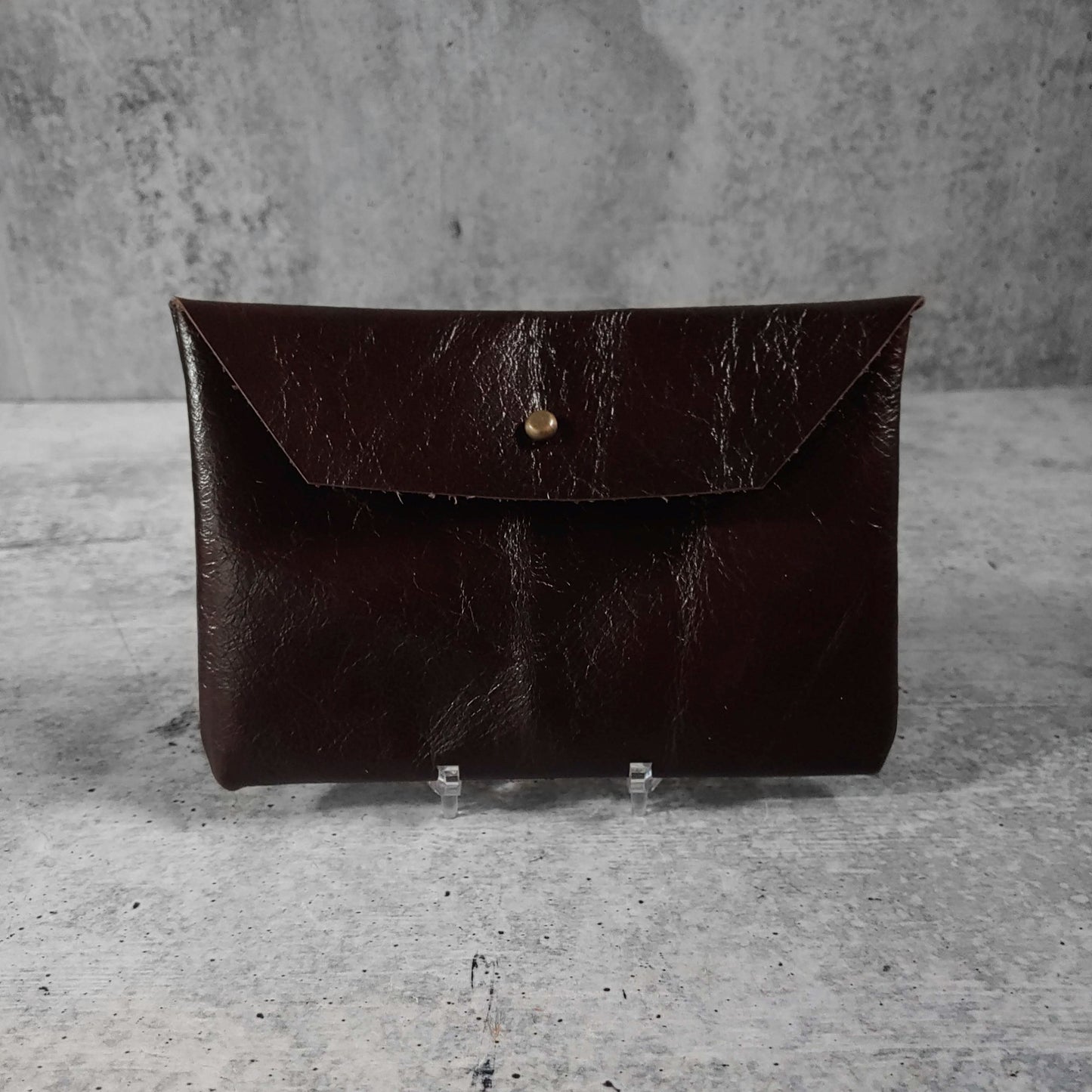 Front facing view of "soft leather clutch trapezoid" in chocolate against a concrete background.