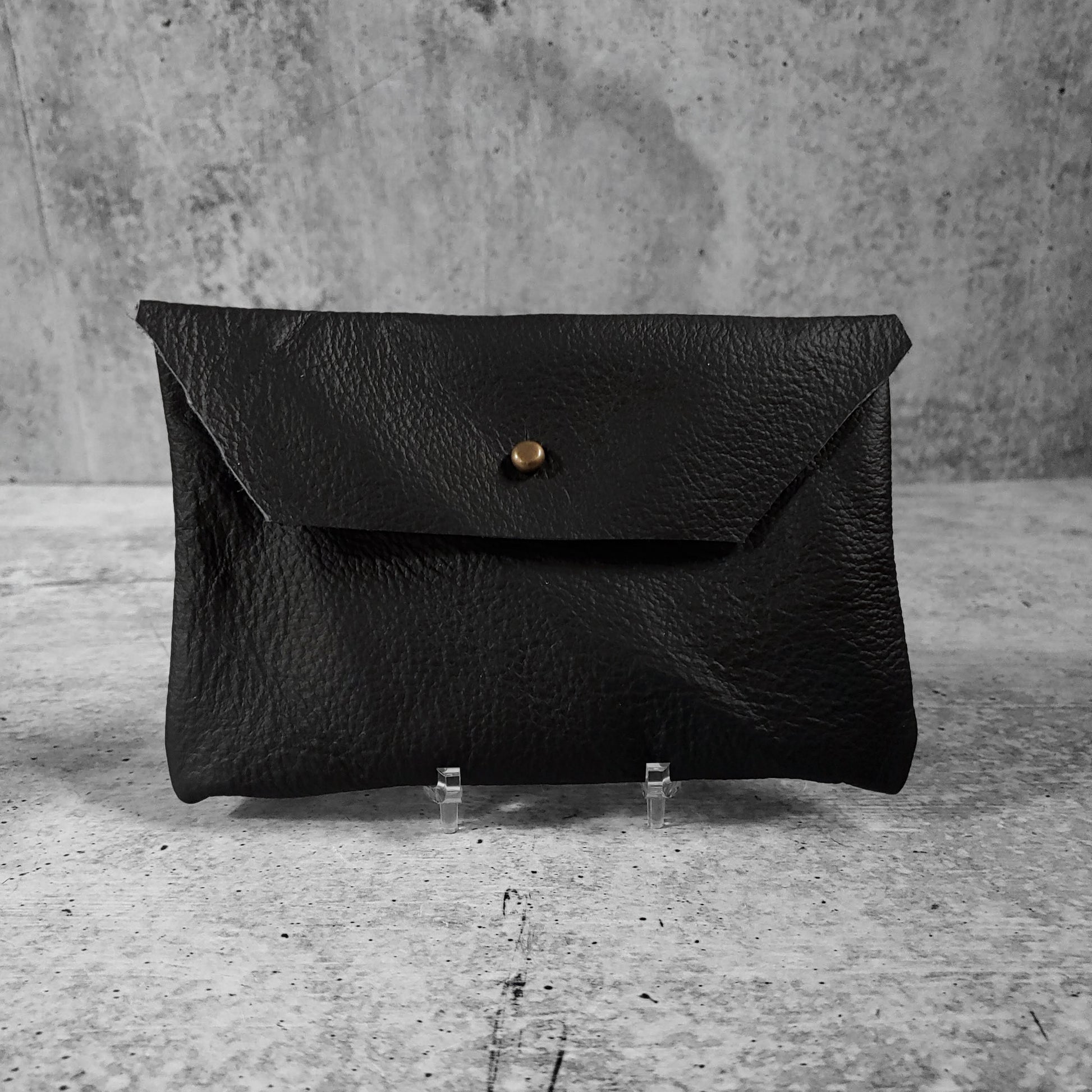 Front facing view of "soft leather clutch trapezoid" in onyx against a concrete background.