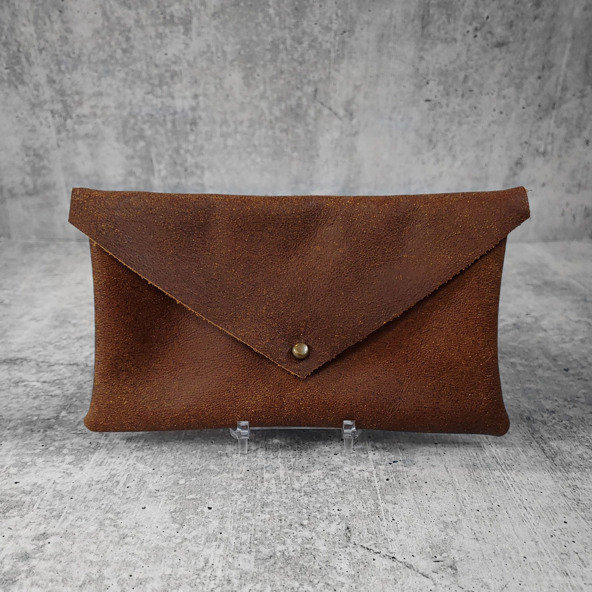 Front facing view of "soft leather clutch triangle" in walnut against a concrete background.