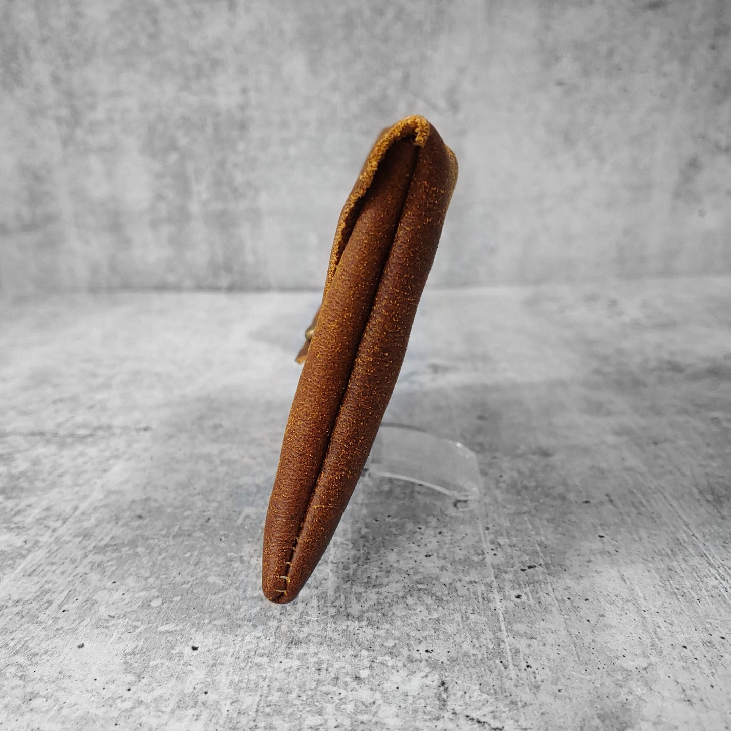 Side view of "soft leather clutch triangle" in walnut against a concrete background.