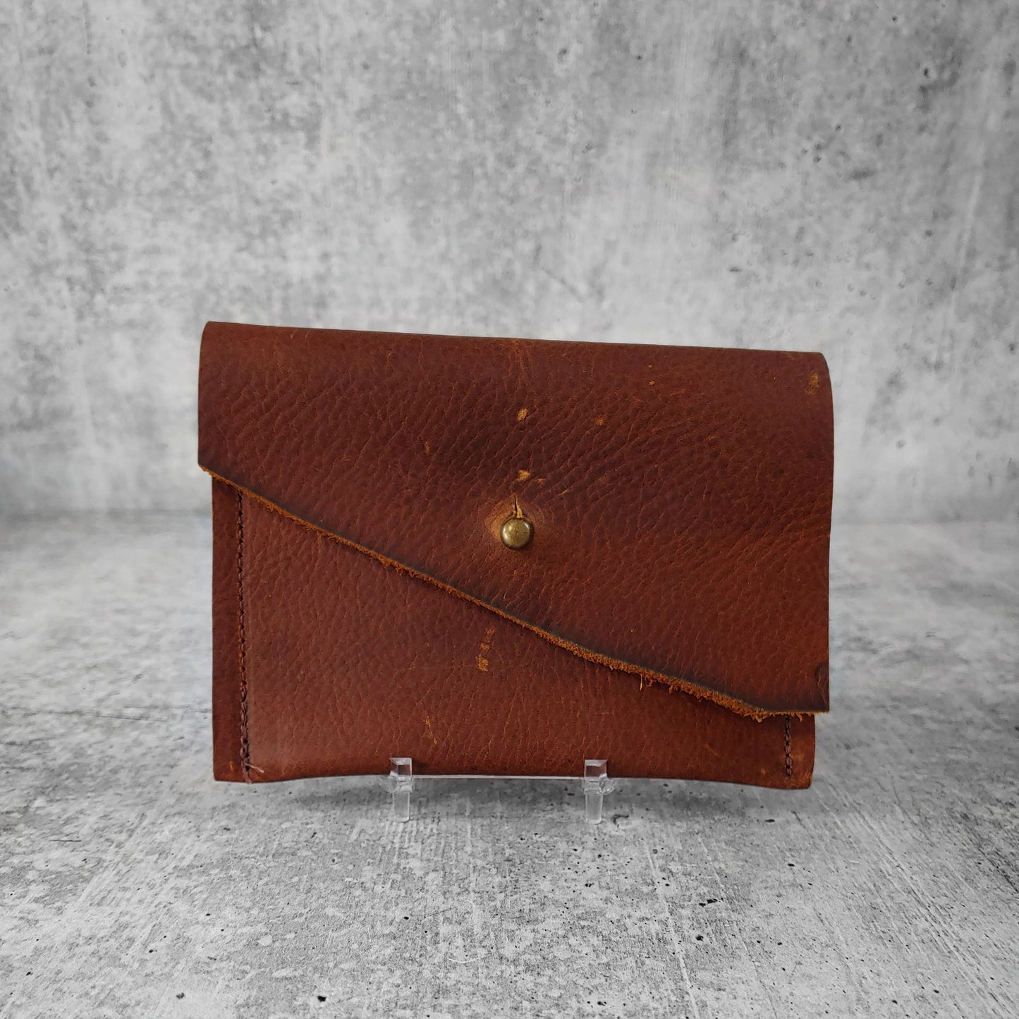 Front facing view of "wide leather wallet with asymmetric flap" in kodiak brown against a concrete background.