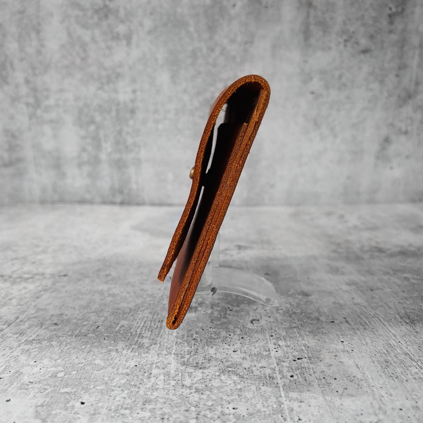 Side view of "wide leather wallet with asymmetric flap" in kodiak brown against a concrete background.