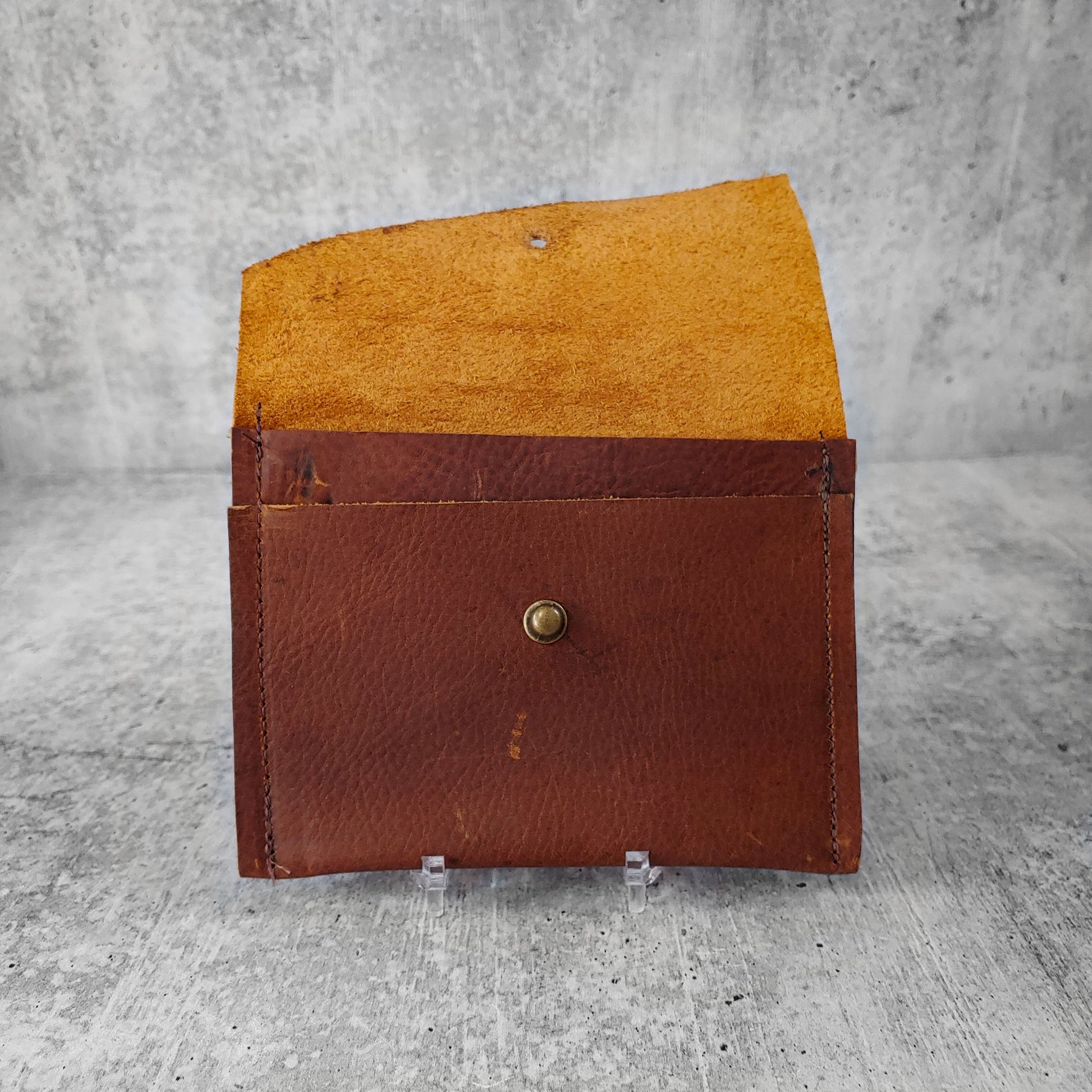 Open, front facing view of "wide leather wallet with asymmetric flap" in kodiak brown against a concrete background. Inside pocket visible.