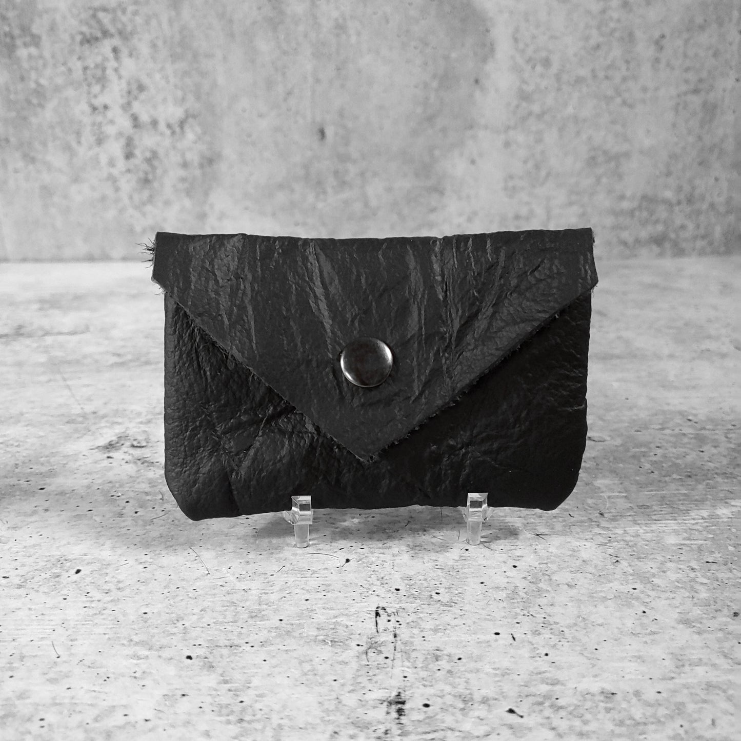 Front facing view of "wrinkled soft leather card holder" in onyx against a concrete background.