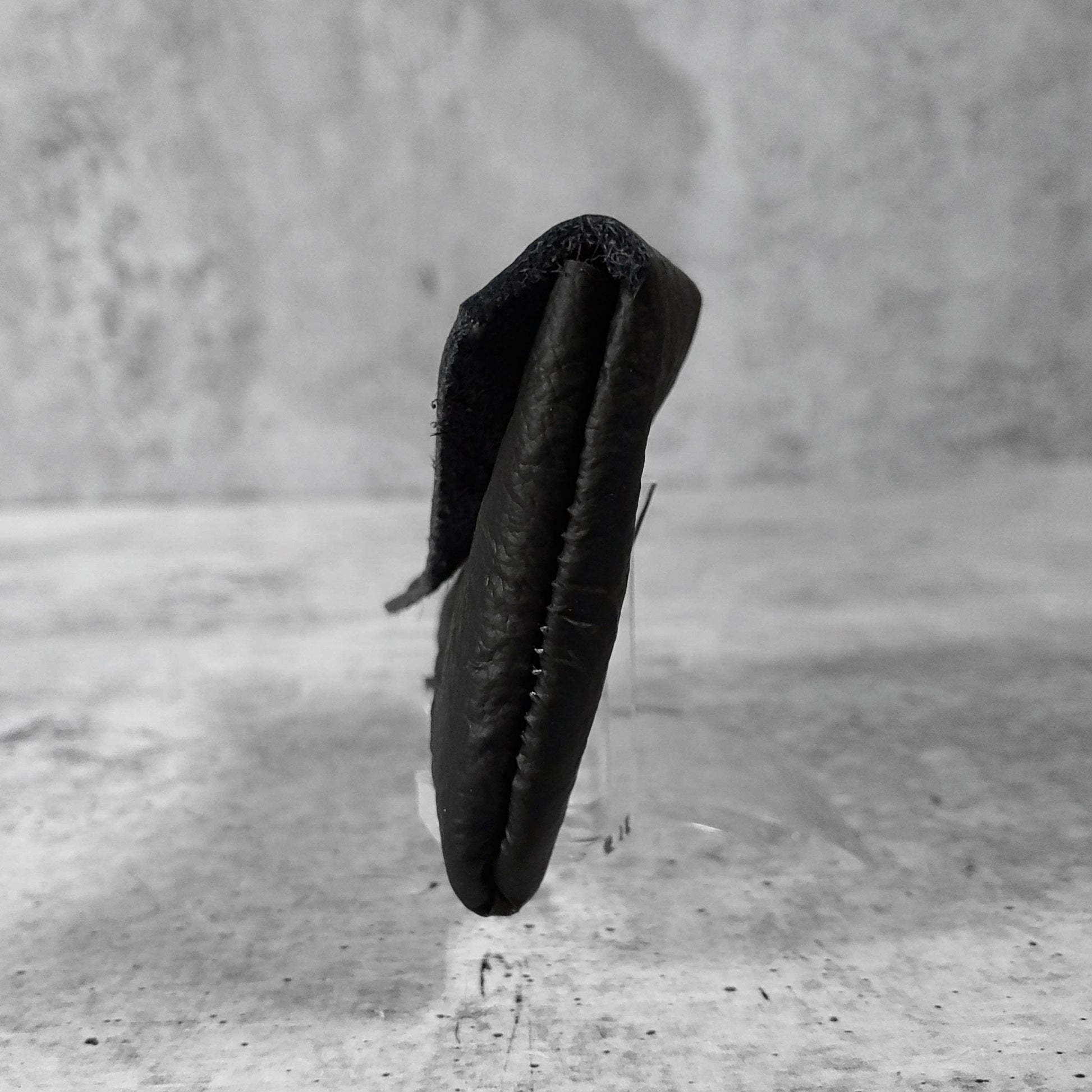 Side view of "wrinkled soft leather card holder" in onyx against a concrete background.