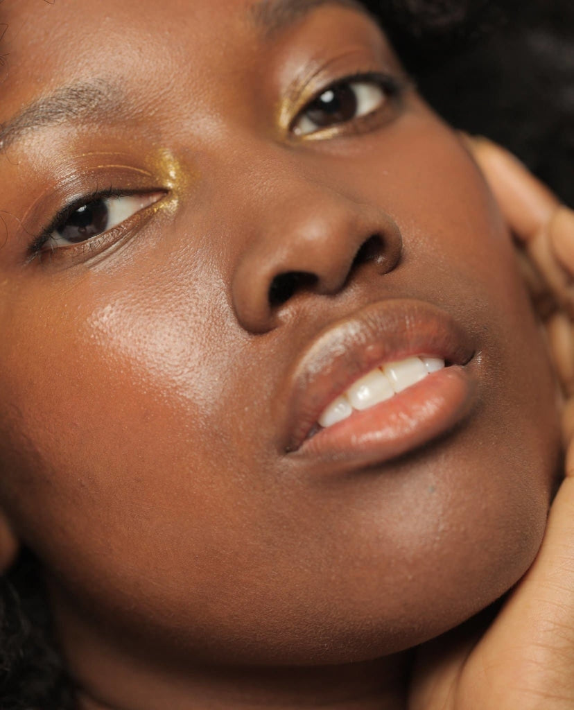 Shimmering golden NOTO Gold Glow Stick product showcased on African American female model, around her eyes.