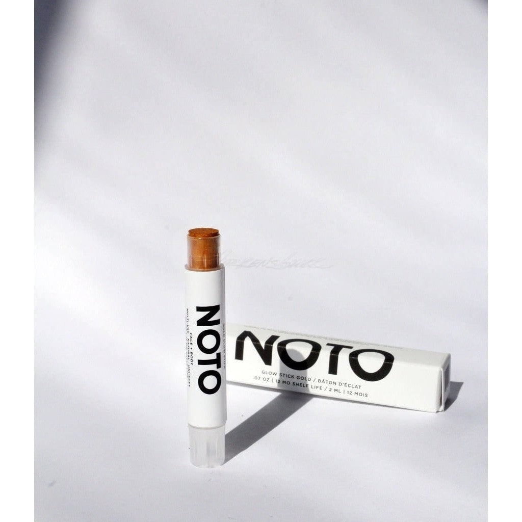 Shimmering golden NOTO Gold Glow Stick displayed next to white product box with black lettering.