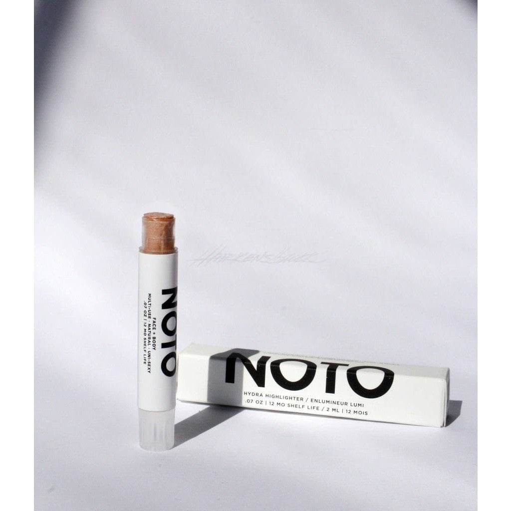 Translucent tan colored NOTO Hydra Highlighter Stick displayed next to white product box with black lettering.