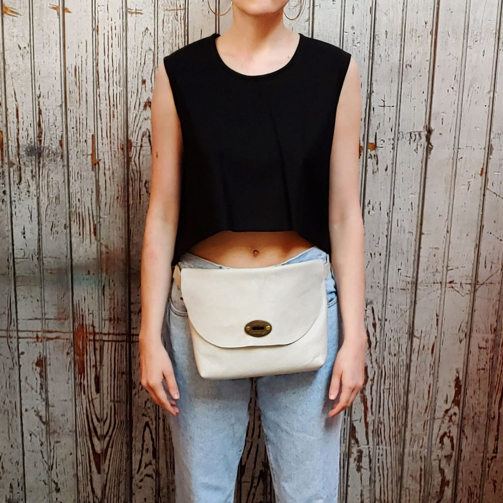 Front view of model wearing "large smooth leather hip bag" in off white against a wood paneled background.