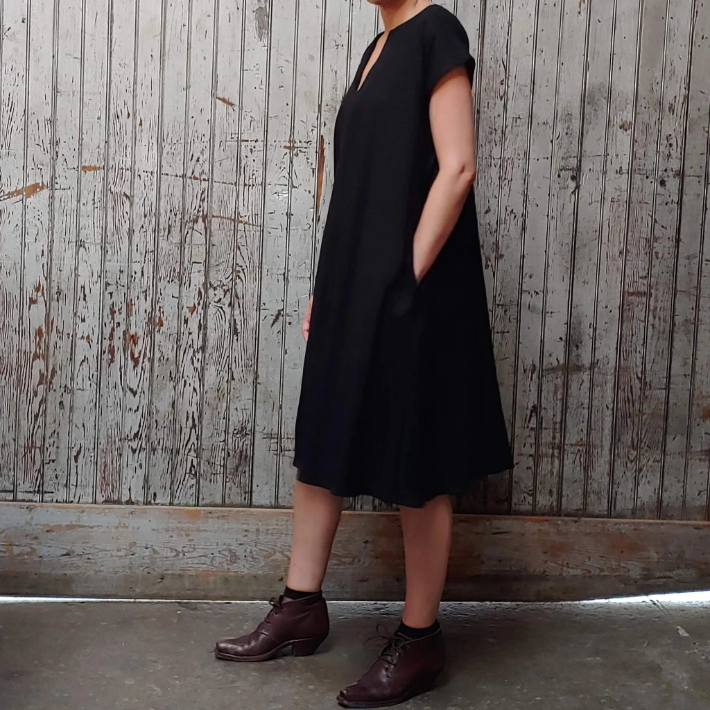 Side view of model wearing McCULLOUGH Morian Midi swing dress in black linen at Harkensback. Hand is in pocket.